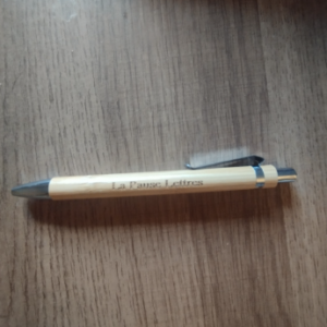 Stylo gravé La Pause Lettres posé sur une table en bois